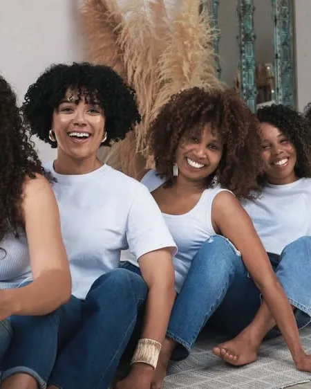Clients with natural curly and coily hair sitting together in jeans, laughing